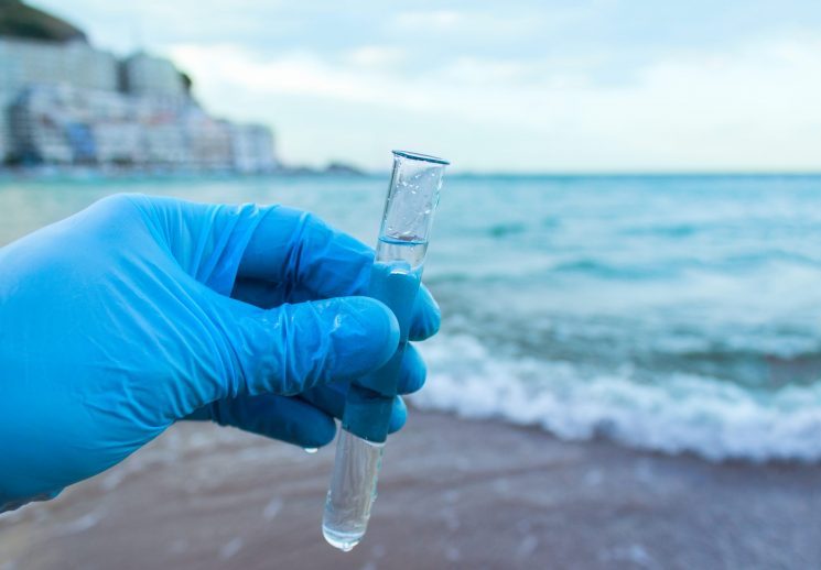Gloved hand holding a water sample at the shoreline